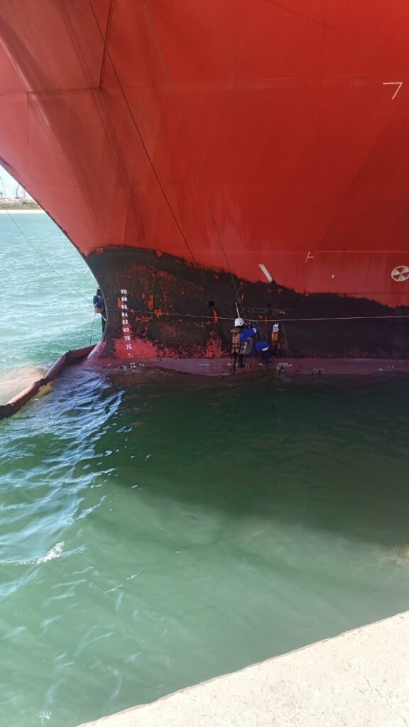 Vista da proa de um navio com t&eacute;cnicos de acesso por corda trabalhando no costado, pr&oacute;ximo &agrave; linha d'&aacute;gua