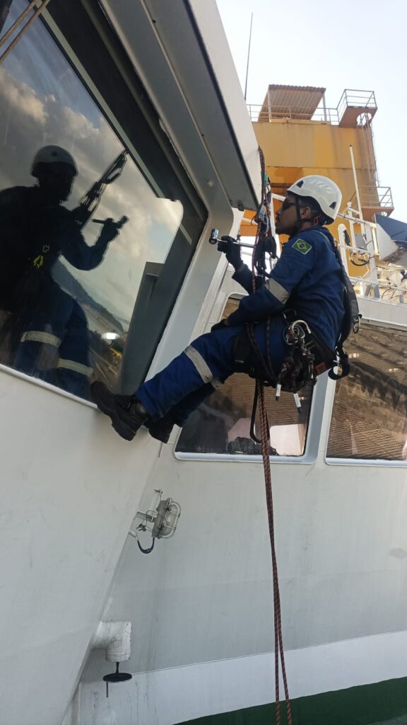 T&eacute;cnico suspenso em corda executando manuten&ccedil;&atilde;o na janela da superestrutura branca do navio